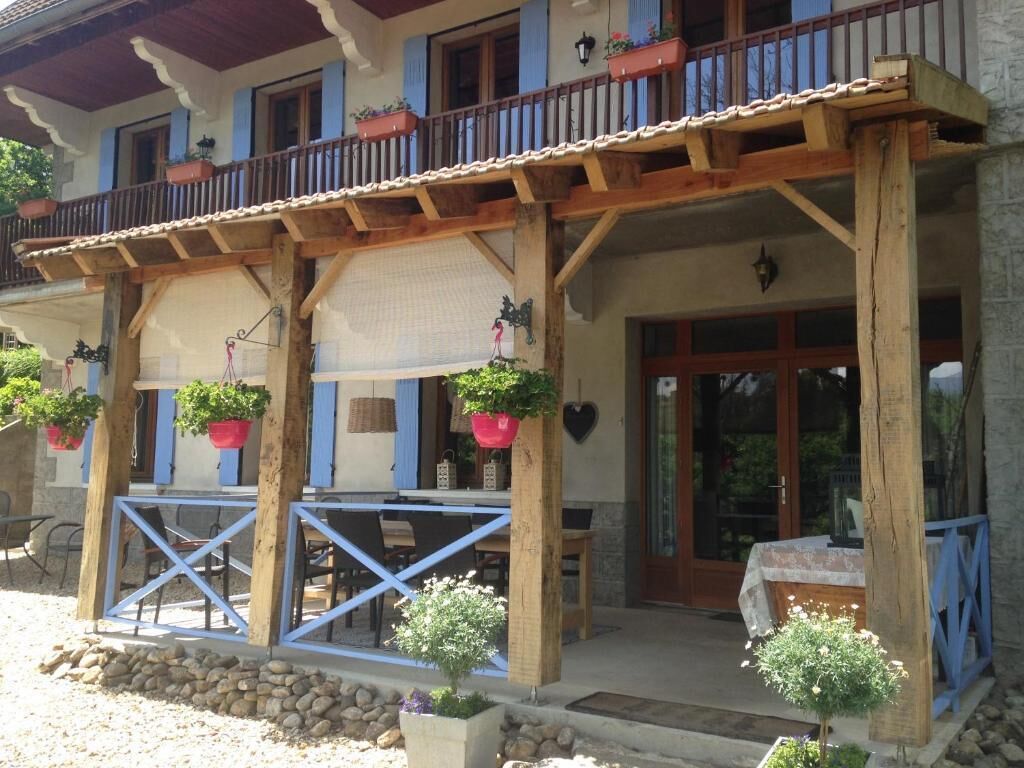 A traditional chalet with a wooden balcony, outdoor seating, and potted plants.