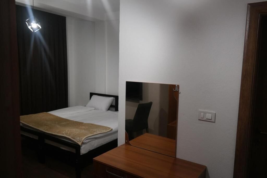 A hotel room with a bed, bedside table, and a mirror.