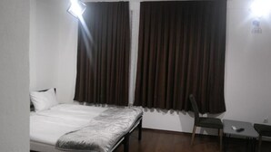 Ein Hotelzimmer mit Bett, Sessel, kleinem Tisch und einem fenster mit Vorhängen.