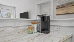 A kitchen with a coffee maker, two jars with lids, and a painting on the wall. - Mid Century Remodeled Suite in Midtown – 20A (Mobile)