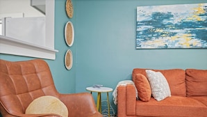 A room with a brown leather armchair, an orange sofa, a small round table, and a wall-mounted shelf. - Mid Century Remodeled Suite in Midtown – 20A (Mobile)