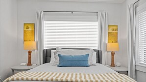 A neatly arranged bedroom with a bed, two bedside tables, a window with blinds, and two wall-mounted lamps. - Mid Century Remodeled Suite in Midtown – 20A (Mobile)