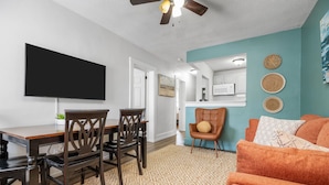 A living room with a TV, a sofa, and a dining area with chairs and a table. - Mid Century Remodeled Suite in Midtown – 20A (Mobile)