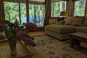 A living room with a sofa, a coffee table, a hanging chair, and a view of a forest through large windows.