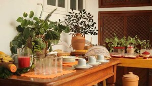 A breakfast table set with plates, cups, and a pitcher of juice, surrounded by potted plants and a rustic wooden table.