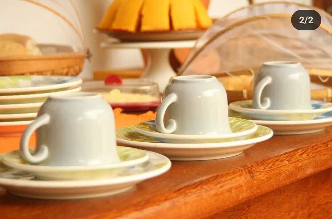 A table with three white cups on saucers, a basket of bread, and a fruit display in the background.
