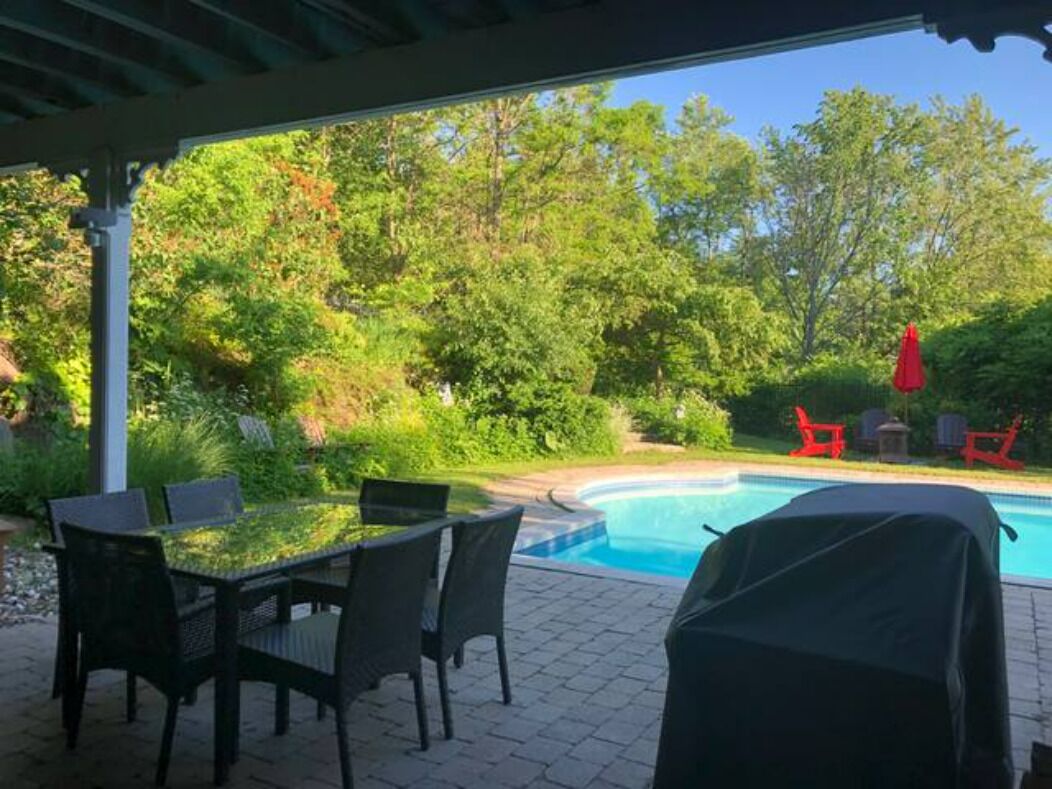 An outdoor patio with a pool, surrounded by greenery and red chairs.