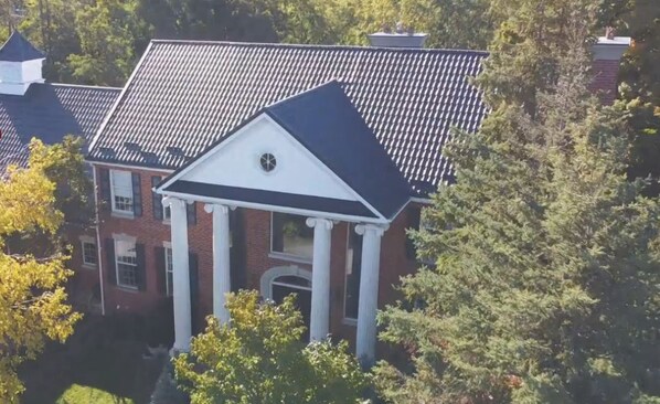 A large, historic building with a symmetrical facade, central columns, and a steeply pitched roof.