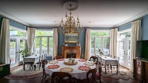 Une salle à manger agrémentée d’un lustre, d’une cheminée et de grandes fenêtres.