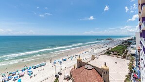 Vista de la playa con un paseo marítimo, sombrillas de playa y un muelle a lo lejos.