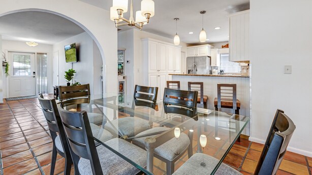 A modern dining area with a glass table and chairs, white cabinets, and pendant lighting. - Heated Pool + Game Room | Near Vanderbilt Beach (Naples)