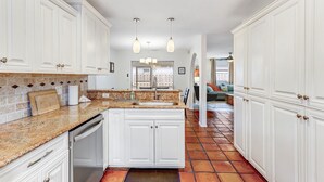 A kitchen with white cabinets, granite countertops, and a tiled floor. - Heated Pool + Game Room | Near Vanderbilt Beach (Naples)