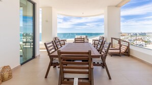 A spacious balcony with a dining table and chairs, offering a view of the ocean and cityscape.