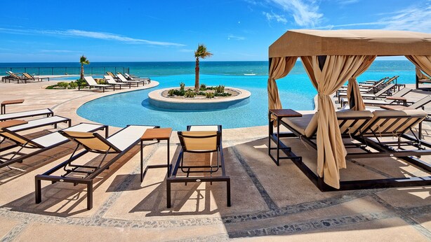 A poolside area with lounge chairs and a canopy, overlooking a clear blue pool and ocean.