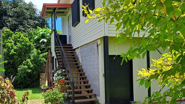 A two-story house with a wooden staircase leading to the second floor, surrounded by a well-maintained garden with various plants and flowers. - Atherton Apartment with Views and Breakfast Hamper (Atherton)