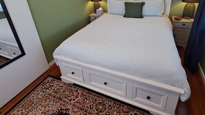 A neatly made bed with a patterned bedspread, a bedside table with a lamp, and a rug on the floor. - Atherton Apartment with Views and Breakfast Hamper (Atherton)
