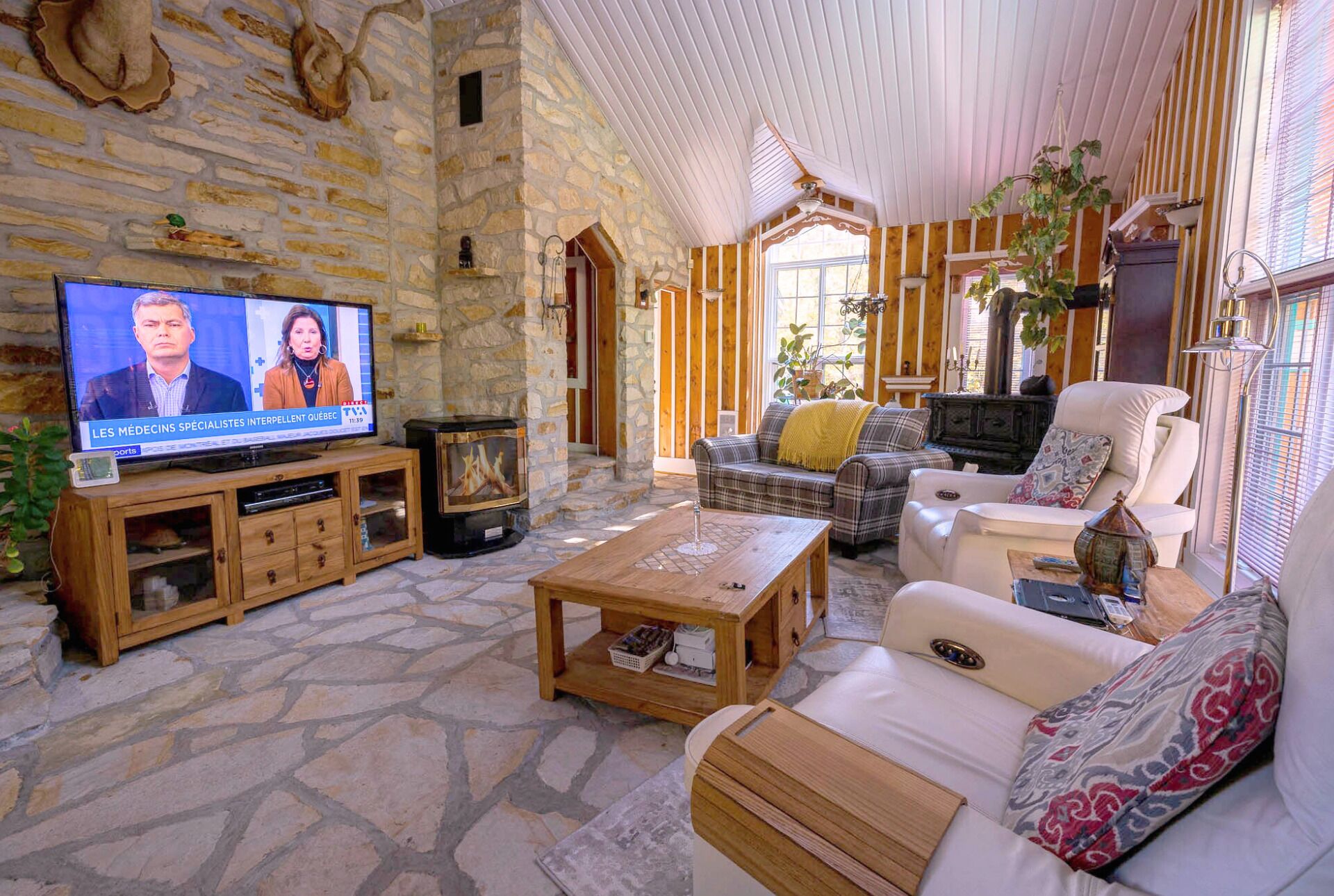A cozy living room with stone walls, wooden furniture, a television, and a fireplace.