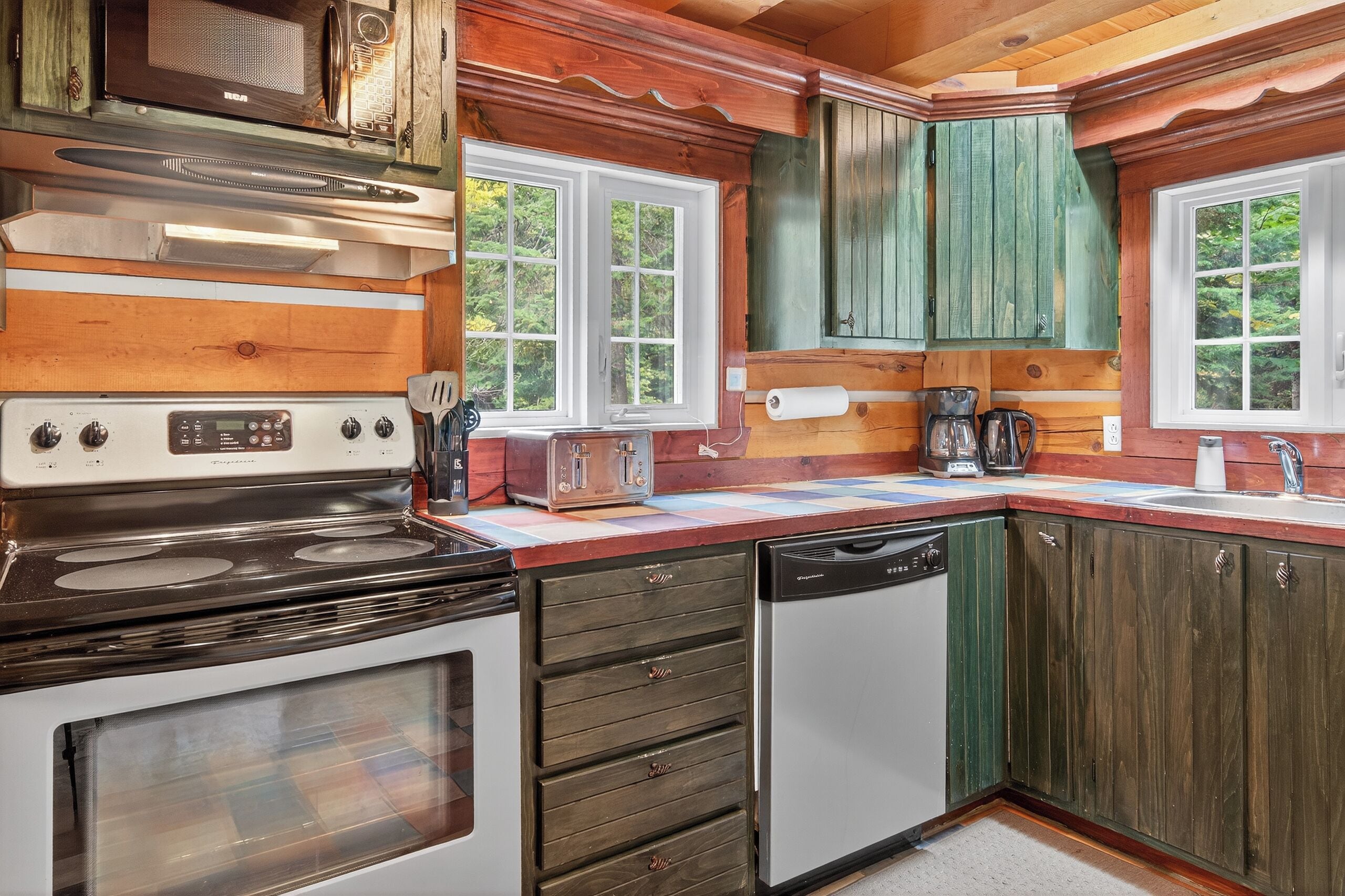 Una cocina con armarios de madera, estufa, lavavajillas y ventana con vistas a zonas verdes.