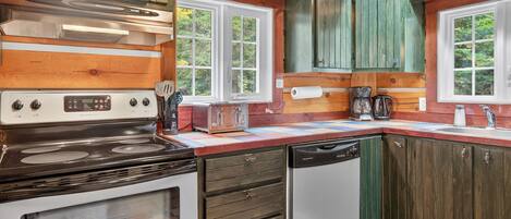 Una cocina con armarios de madera, estufa, lavavajillas y ventana con vistas a zonas verdes.