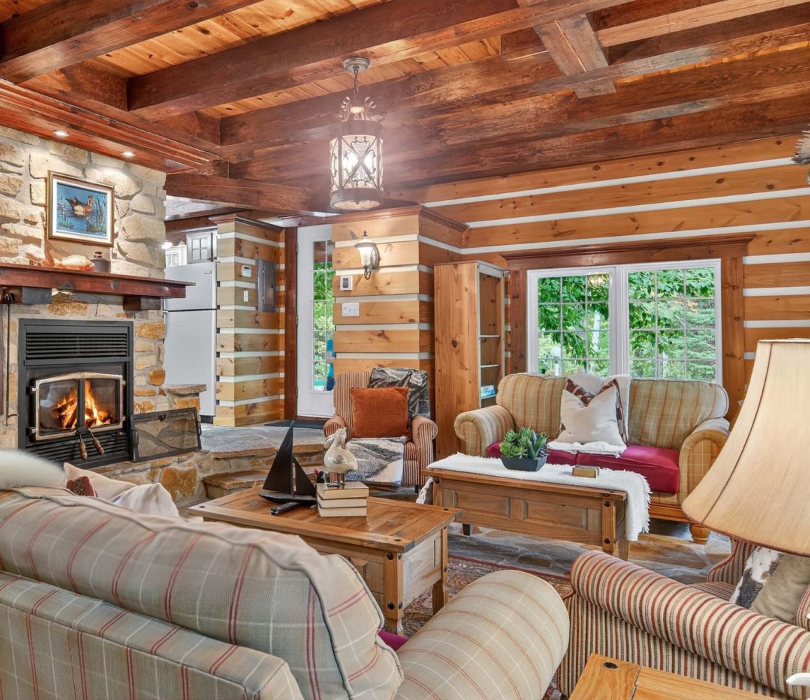 A cozy log cabin interior with a stone fireplace, a television, and comfortable seating.