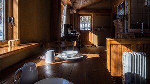 Un interior de madera con una mesa de comedor, sillas, una tetera, una cafetera y un radiador.