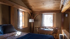 Una habitación de cabaña de madera con una cama, una mesa, sillas y una ventana.