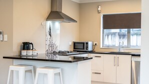 A modern kitchen with a central island, white bar stools, a microwave, a coffee maker, and a stainless steel dishwasher. - Natural touch (Hamilton)