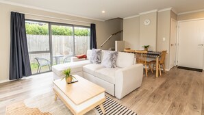 A modern living room with a white sofa, a wooden coffee table, and a dining area with a table and chairs. - Natural touch (Hamilton)