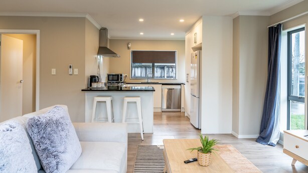 A modern kitchen with a central island, white bar stools, and a large window. - Natural touch (Hamilton)