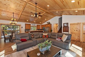 A spacious living room with a large sectional sofa, a coffee table with a plant centerpiece, and a wooden ceiling with exposed beams. - Charming Summit Cabin-Hot Tub-5 Min Walk To Slopes (Big Bear Lake)