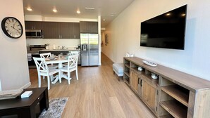 Eine moderne Küche mit Essbereich, Holzschränken, einem Edelstahlkühlschrank und einem flachbildfernseher an der Wand.
