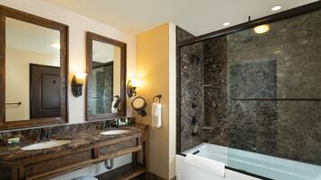 A bathroom with a large mirror, two sinks, a bathtub, and a glass-enclosed shower.