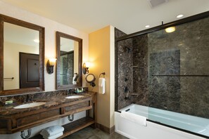 A bathroom with a large mirror, two sinks, a bathtub, and a glass-enclosed shower.