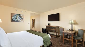 A hotel room with a bed, a desk, a chair, a lamp, a television, and a painting on the wall.