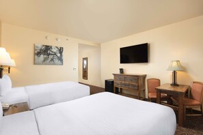A hotel room with two beds, a TV, a desk with a lamp, a chair, and a small table.