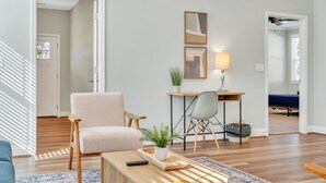 Ein Wohnzimmer mit Sofa, Couchtisch, Schreibtisch mit Stuhl, Lampe und Pflanze.