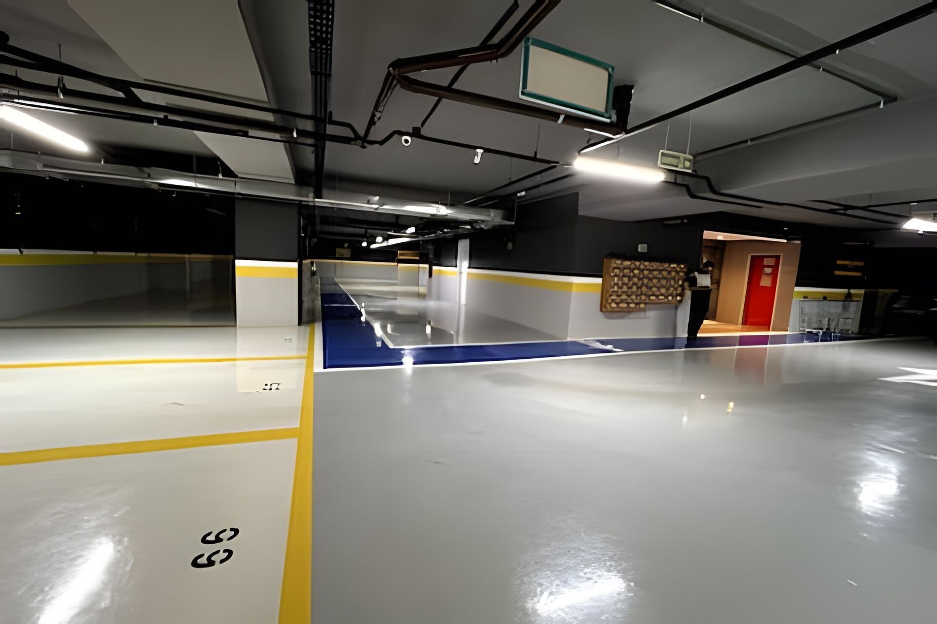 A spacious indoor parking area with clear markings on the floor, a red exit door, and a wall-mounted information board.