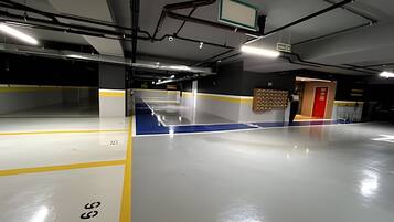 A spacious indoor parking area with clear markings on the floor, a red exit door, and a wall-mounted information board.
