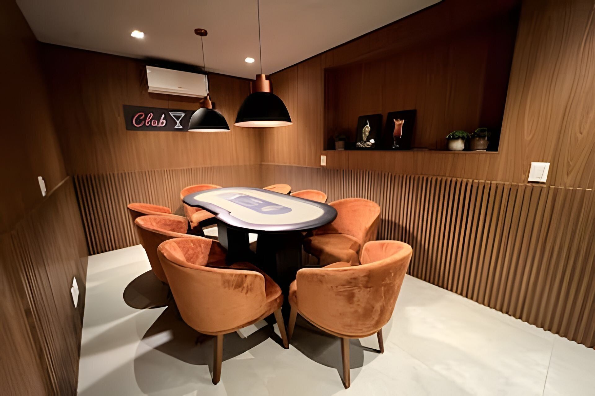 A conference room with a round table, six orange chairs, two pendant lights, and wooden paneling on the walls.
