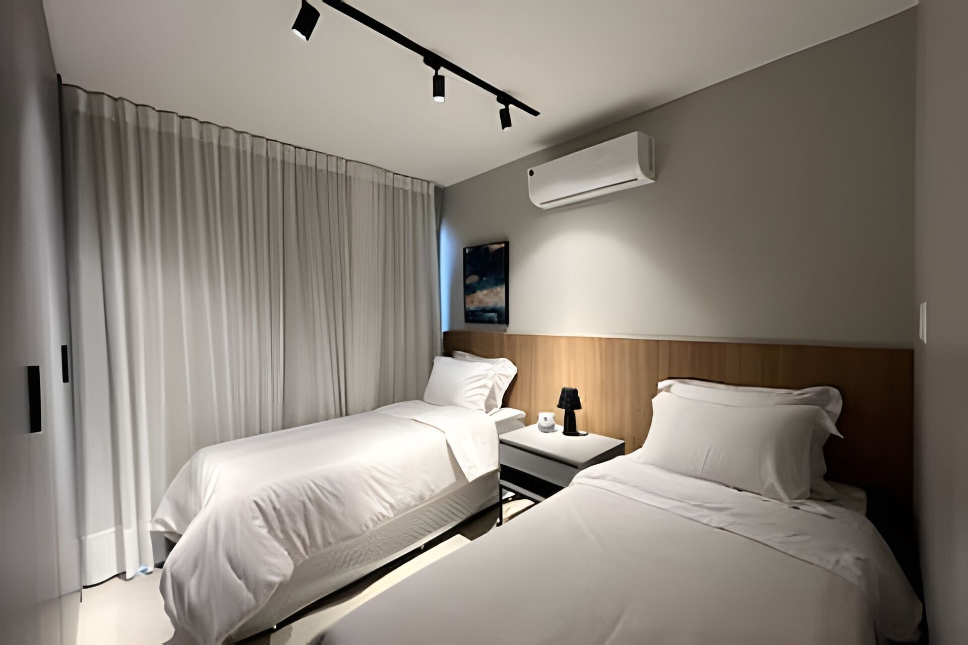 A hotel room with two beds, a nightstand, an air conditioning unit, and a painting on the wall.