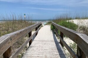 Una passerella di legno che conduce a una spiaggia con dune di sabbia e una vista limpida sull'oceano.
