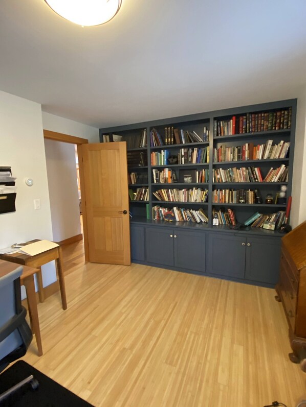 Ein Zimmer mit Holzboden, einem Schreibtisch mit Stuhl und einem großen Bücherregal, gefüllt mit Büchern.