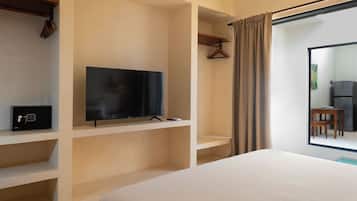 A hotel room with a bed, a television on a shelf, a coat rack, and a view of a kitchen area.