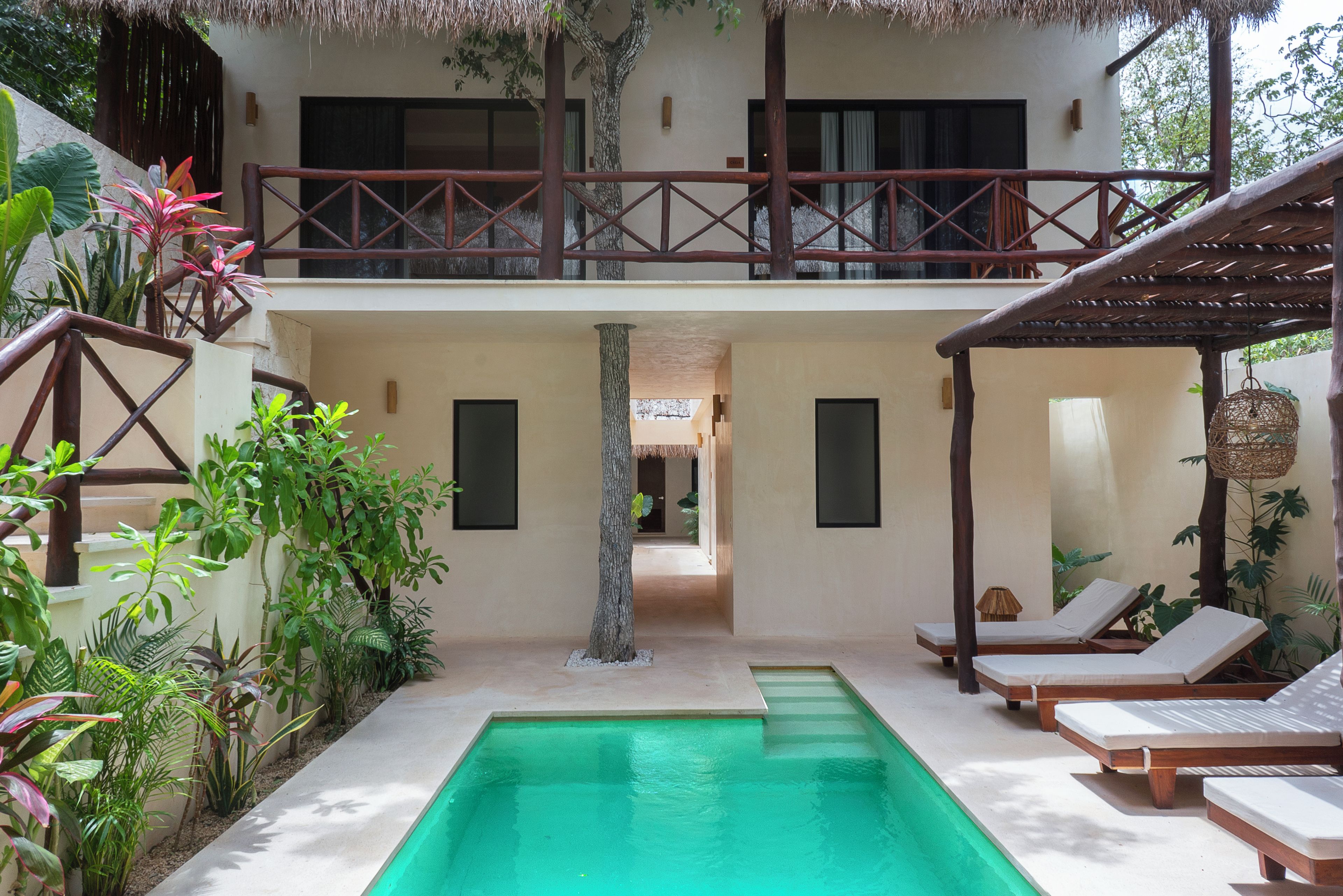 Un área de piscina con piscina azul cristalina, sillas de descanso y una pérgola de madera.