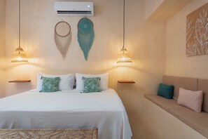 A hotel room with a bed, two wall-mounted lamps, a wall air conditioner, and a wall art piece.