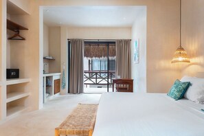 A hotel room with a bed, a desk, a chair, a hanging light fixture, and a view through a glass door. - Casa Yaakun (Tulum)