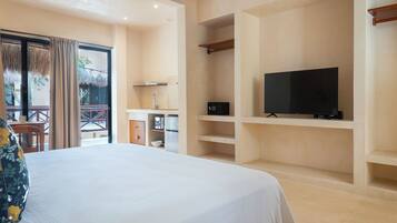 A hotel room with a bed, a television on a shelf, a small kitchen area, and a balcony with a table and chairs.