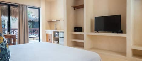 A hotel room with a bed, a television on a shelf, a small kitchen area, and a balcony with a table and chairs.