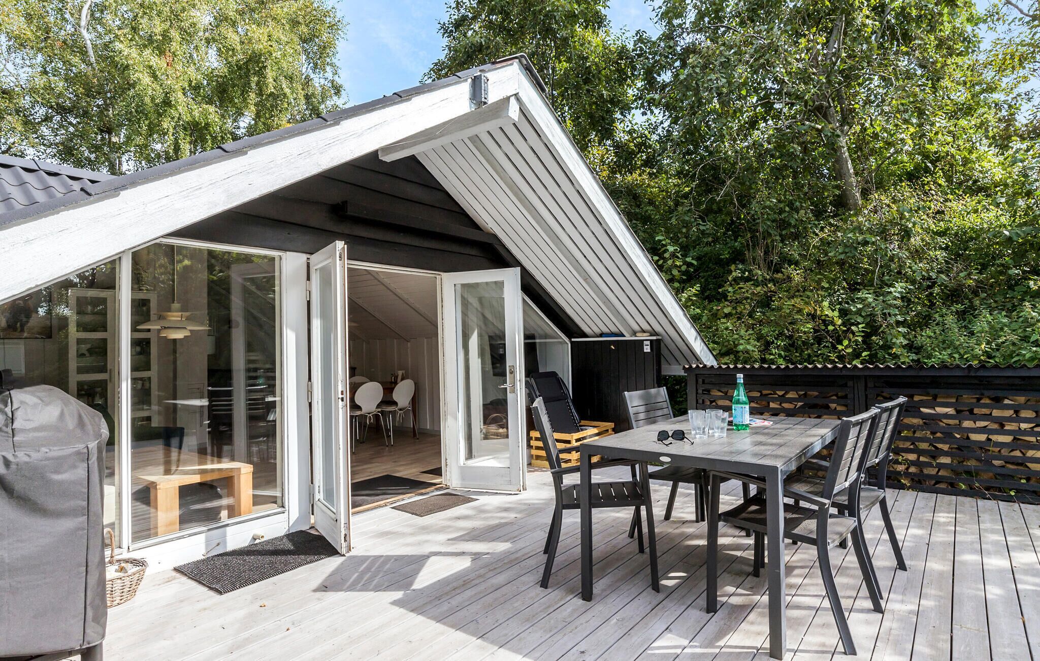 A modern outdoor deck with a dining table and chairs, a grill, and a glass door leading to an interior space.