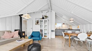 A spacious loft with a high ceiling, a cozy living area with a sofa, a blue armchair, and a dining table with chairs.